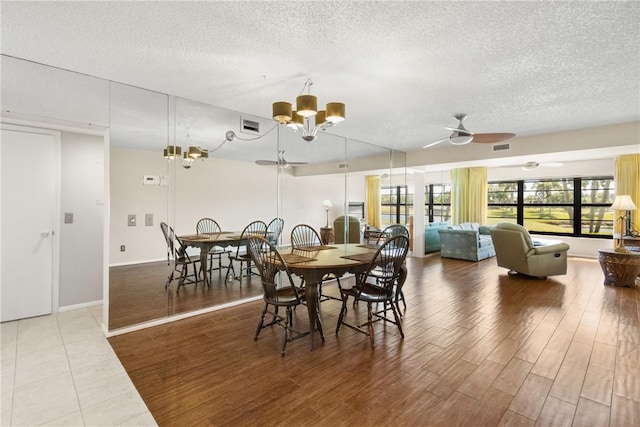 dining space featuring visible vents, wood finished floors, baseboards, a textured ceiling, and ceiling fan with notable chandelier