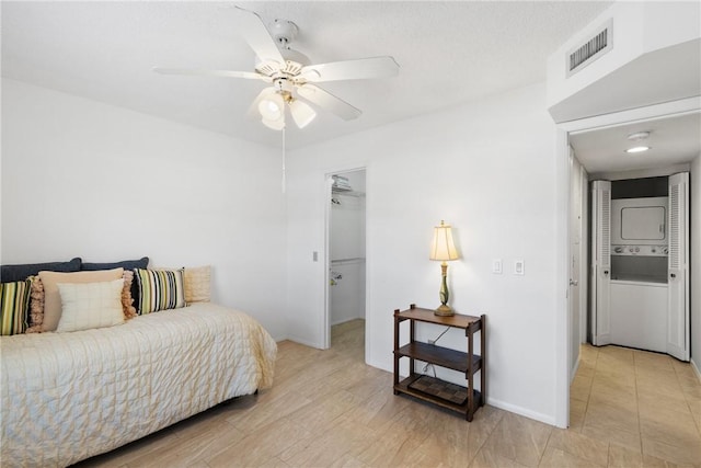 bedroom featuring a walk in closet, a ceiling fan, visible vents, stacked washer / drying machine, and baseboards
