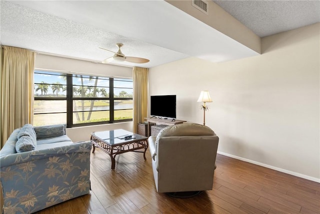 living area with wood finished floors, ceiling fan, a textured ceiling, and visible vents