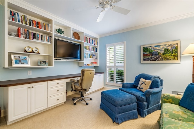 carpeted home office with built in desk, ceiling fan, and crown molding