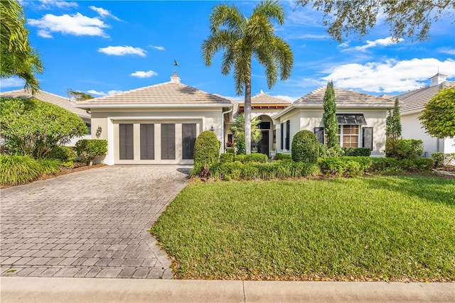 ranch-style home featuring decorative driveway, stucco siding, an attached garage, a tiled roof, and a front lawn