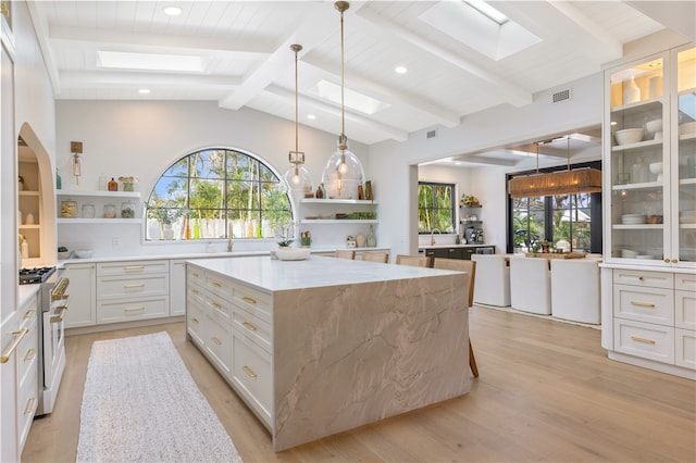 kitchen featuring light hardwood / wood-style floors, white cabinetry, light stone counters, a center island, and stainless steel stove