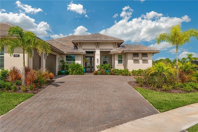 view of front of house with a garage, decorative driveway, stucco siding, french doors, and a tiled roof