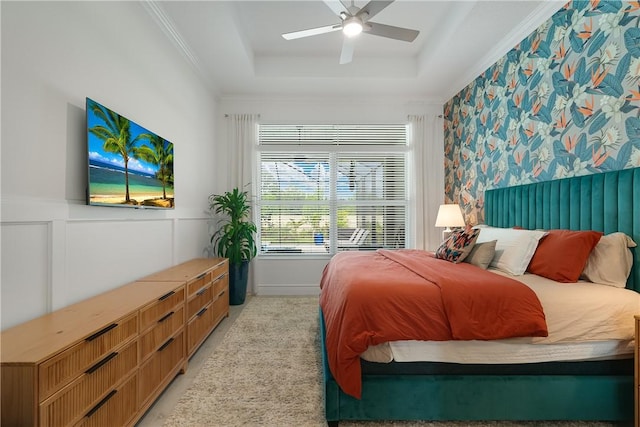 bedroom with a tray ceiling, ceiling fan, a wainscoted wall, and crown molding