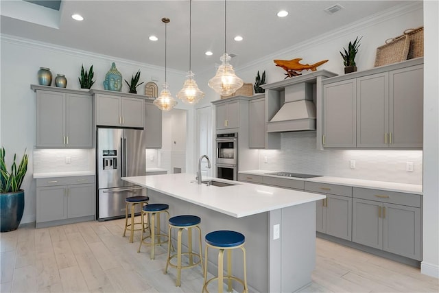 kitchen featuring appliances with stainless steel finishes, gray cabinets, premium range hood, a breakfast bar, and a sink