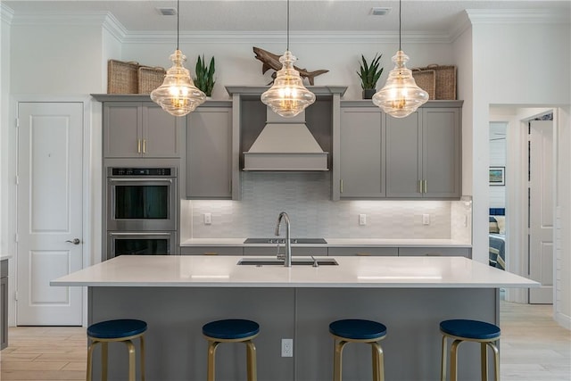 kitchen with double oven, gray cabinets, light wood-style flooring, custom range hood, and ornamental molding