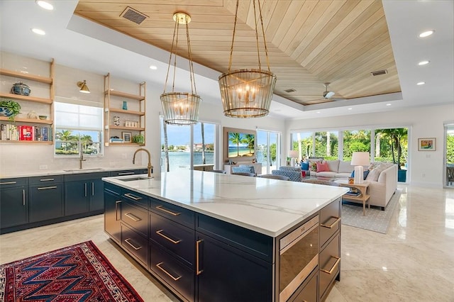 kitchen with a raised ceiling, a kitchen island with sink, sink, and wooden ceiling