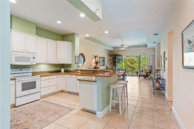 kitchen featuring white appliances, light tile patterned floors, a peninsula, a sink, and white cabinets