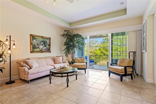 living area featuring light tile patterned floors, baseboards, a tray ceiling, and a ceiling fan