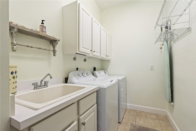 clothes washing area with a sink, washing machine and dryer, cabinet space, light tile patterned flooring, and baseboards