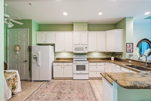 kitchen with dark stone counters, a peninsula, white cabinets, white appliances, and a sink