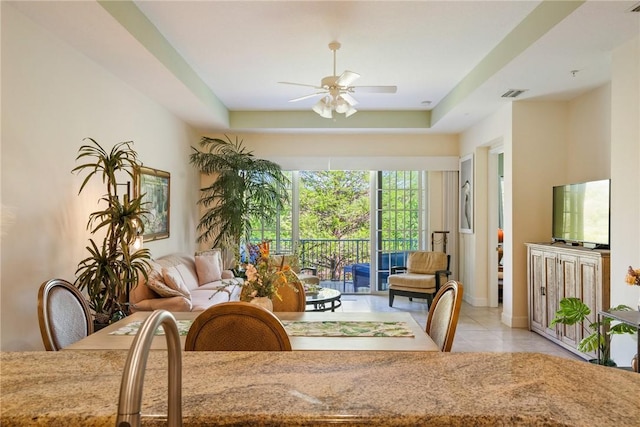 tiled dining room with visible vents, a tray ceiling, and a ceiling fan