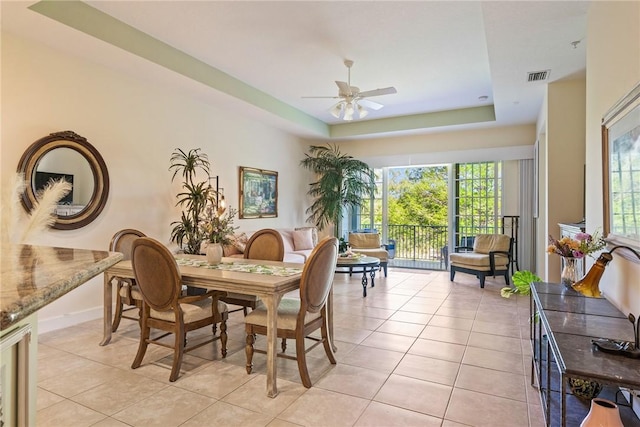 dining room featuring a tray ceiling, plenty of natural light, a ceiling fan, and light tile patterned flooring