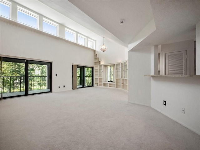 unfurnished living room featuring french doors, carpet floors, a wealth of natural light, and a towering ceiling