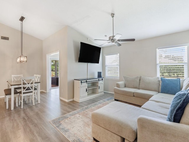 living room featuring lofted ceiling, ceiling fan with notable chandelier, and light hardwood / wood-style floors