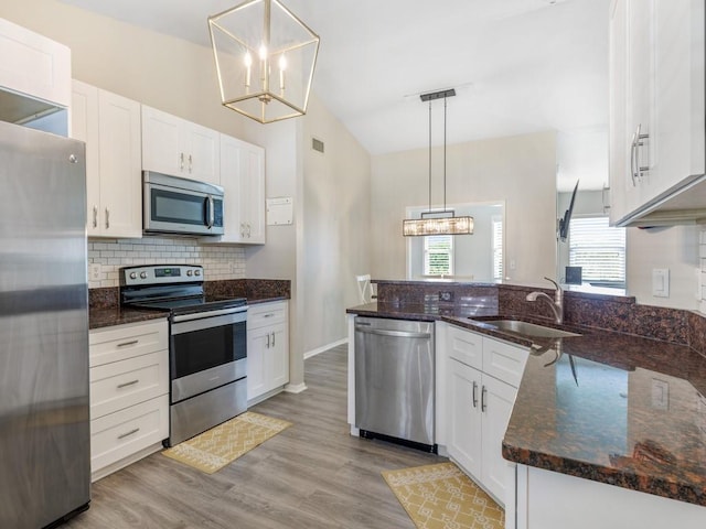 kitchen with appliances with stainless steel finishes, pendant lighting, white cabinetry, dark stone countertops, and a notable chandelier