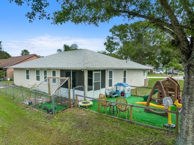 rear view of property with a sunroom, a playground, and a lawn