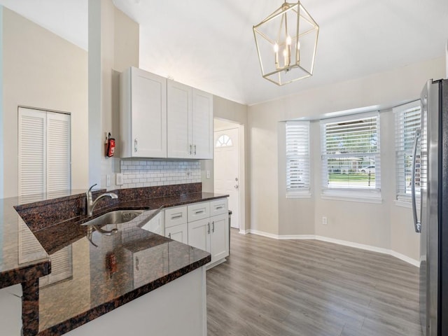 kitchen featuring sink, white cabinetry, hanging light fixtures, stainless steel fridge, and dark stone counters