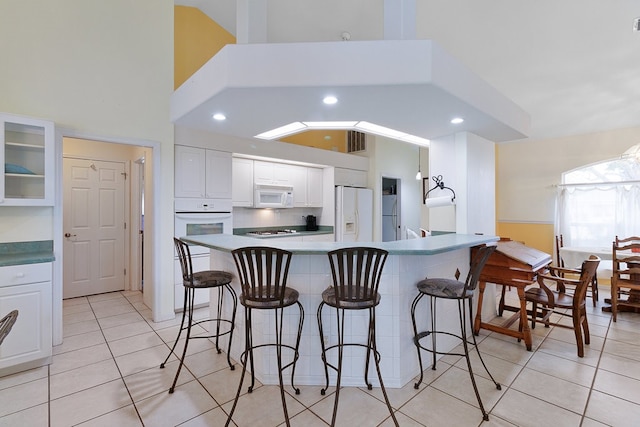 kitchen with white cabinets, white appliances, a kitchen bar, and light tile patterned floors