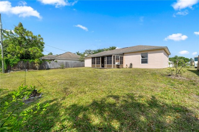 rear view of house with a lawn, stucco siding, a sunroom, and fence private yard