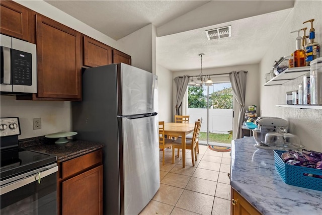 kitchen with appliances with stainless steel finishes, a notable chandelier, light tile patterned flooring, decorative light fixtures, and dark stone counters