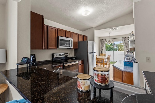 kitchen with lofted ceiling, appliances with stainless steel finishes, hanging light fixtures, a textured ceiling, and dark stone counters