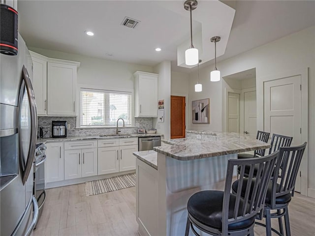 kitchen with a kitchen island, a breakfast bar, white cabinets, light stone counters, and stainless steel appliances