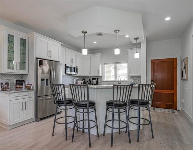 kitchen with stainless steel appliances, pendant lighting, white cabinets, and light stone counters