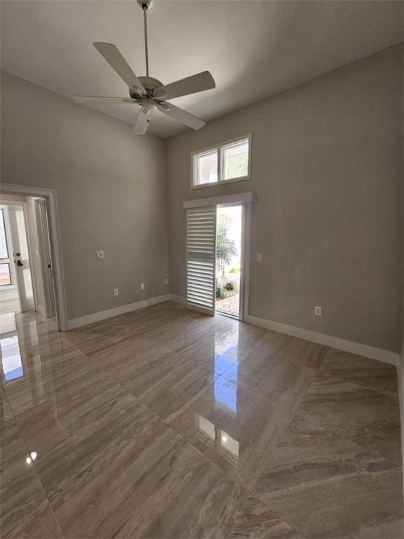 unfurnished room with marble finish floor, a high ceiling, a ceiling fan, and baseboards