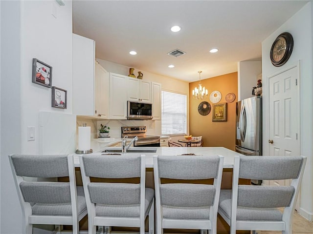 kitchen with a kitchen bar, a chandelier, hanging light fixtures, appliances with stainless steel finishes, and kitchen peninsula