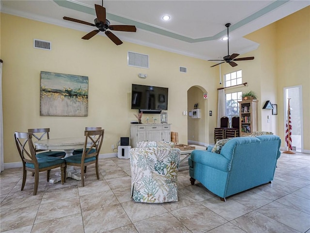 living room with a raised ceiling, ornamental molding, a towering ceiling, and ceiling fan