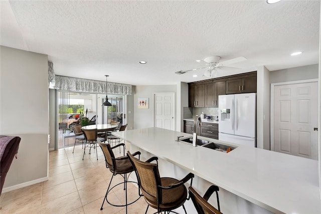 kitchen with dark brown cabinets, ceiling fan, sink, pendant lighting, and white fridge with ice dispenser