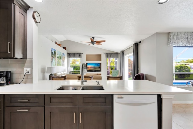 kitchen with sink, white dishwasher, a textured ceiling, vaulted ceiling, and light tile patterned flooring