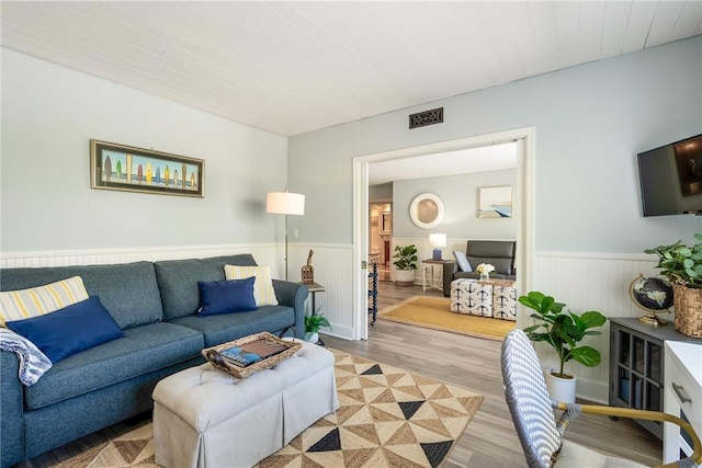 living room featuring a wainscoted wall, light wood-style flooring, and visible vents