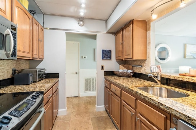 kitchen featuring visible vents, backsplash, appliances with stainless steel finishes, a sink, and light stone countertops