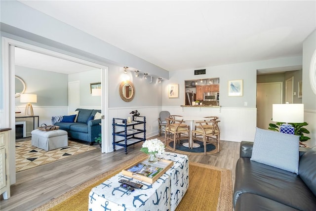 living room with a wainscoted wall, visible vents, and wood finished floors