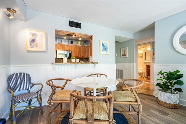 dining area with a wainscoted wall, visible vents, and wood finished floors