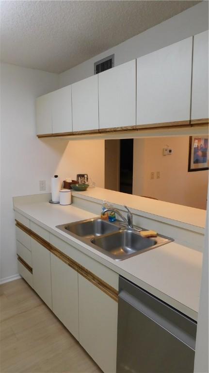 kitchen featuring white cabinets, a textured ceiling, stainless steel dishwasher, and sink