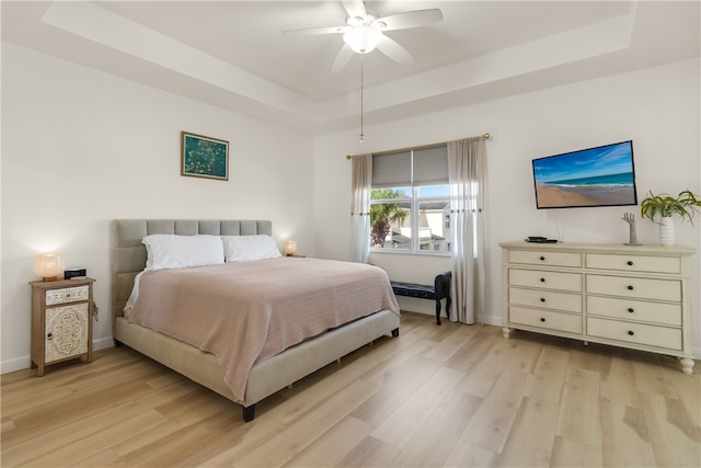 bedroom with ceiling fan, a raised ceiling, and light wood-type flooring