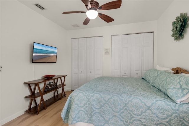 bedroom with light hardwood / wood-style floors, ceiling fan, and two closets