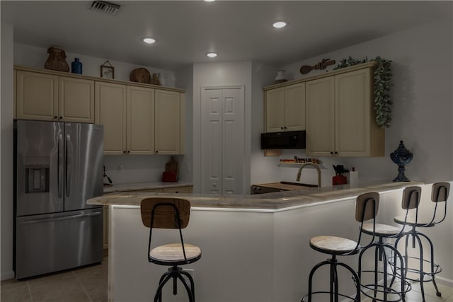 kitchen with stainless steel refrigerator with ice dispenser, light tile patterned floors, cream cabinetry, and a breakfast bar area