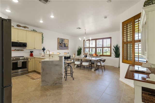 kitchen with a breakfast bar, appliances with stainless steel finishes, cream cabinets, a chandelier, and pendant lighting