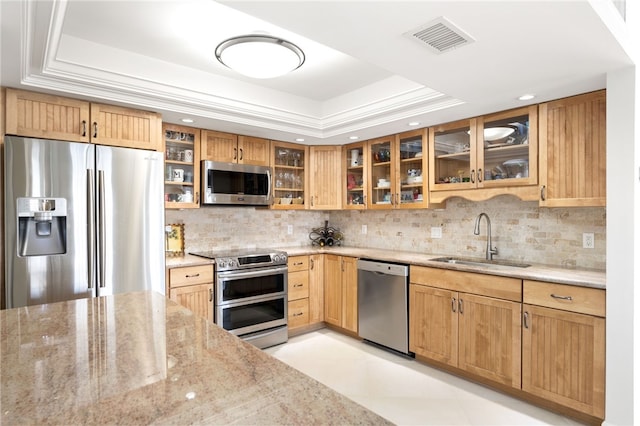 kitchen featuring appliances with stainless steel finishes, light stone counters, a raised ceiling, and sink