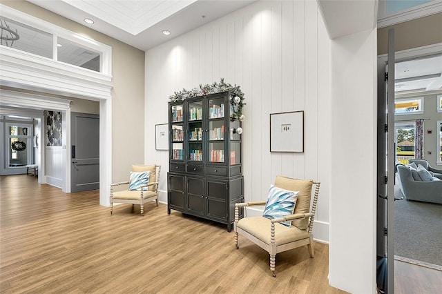 living area featuring light hardwood / wood-style flooring, ornamental molding, and wooden walls