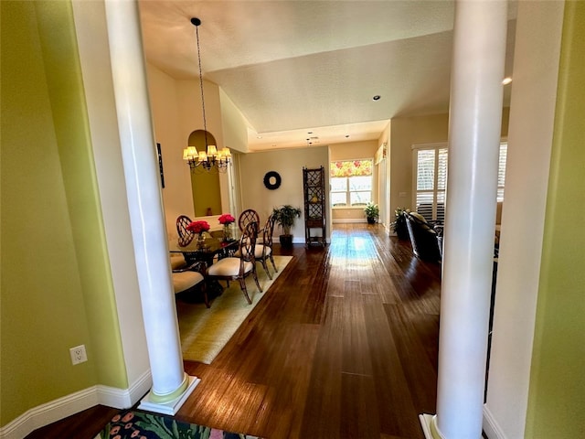 hall with hardwood / wood-style flooring, a notable chandelier, ornate columns, and vaulted ceiling