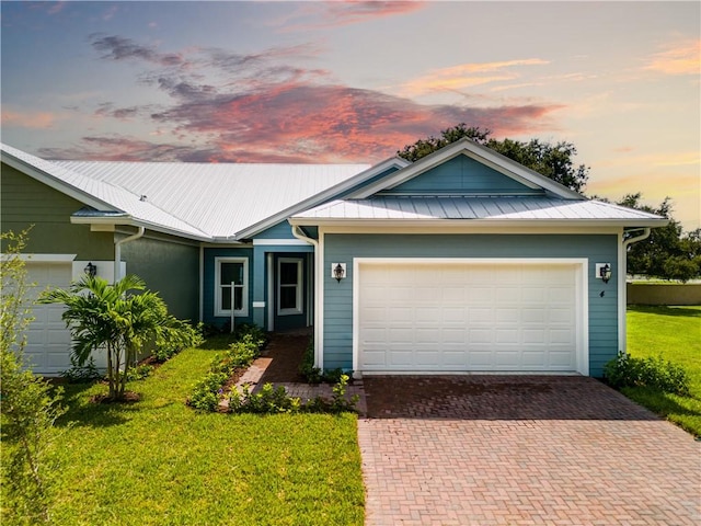 ranch-style home featuring a yard, decorative driveway, metal roof, and an attached garage