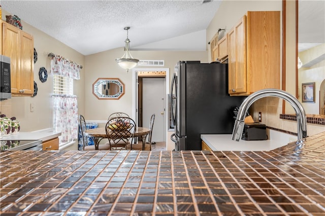 kitchen featuring light brown cabinetry, lofted ceiling, appliances with stainless steel finishes, and hanging light fixtures