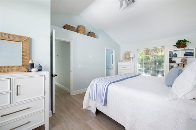 bedroom with ensuite bathroom, light wood-type flooring, and vaulted ceiling