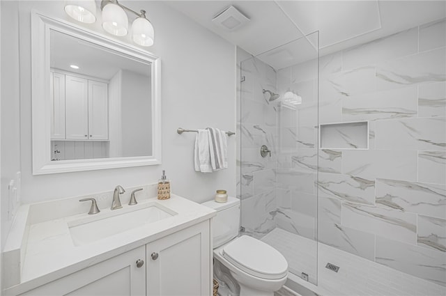 bathroom with toilet, a tile shower, and vanity