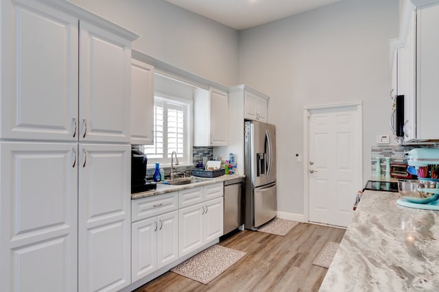 kitchen featuring decorative backsplash, appliances with stainless steel finishes, light stone counters, light hardwood / wood-style floors, and white cabinetry